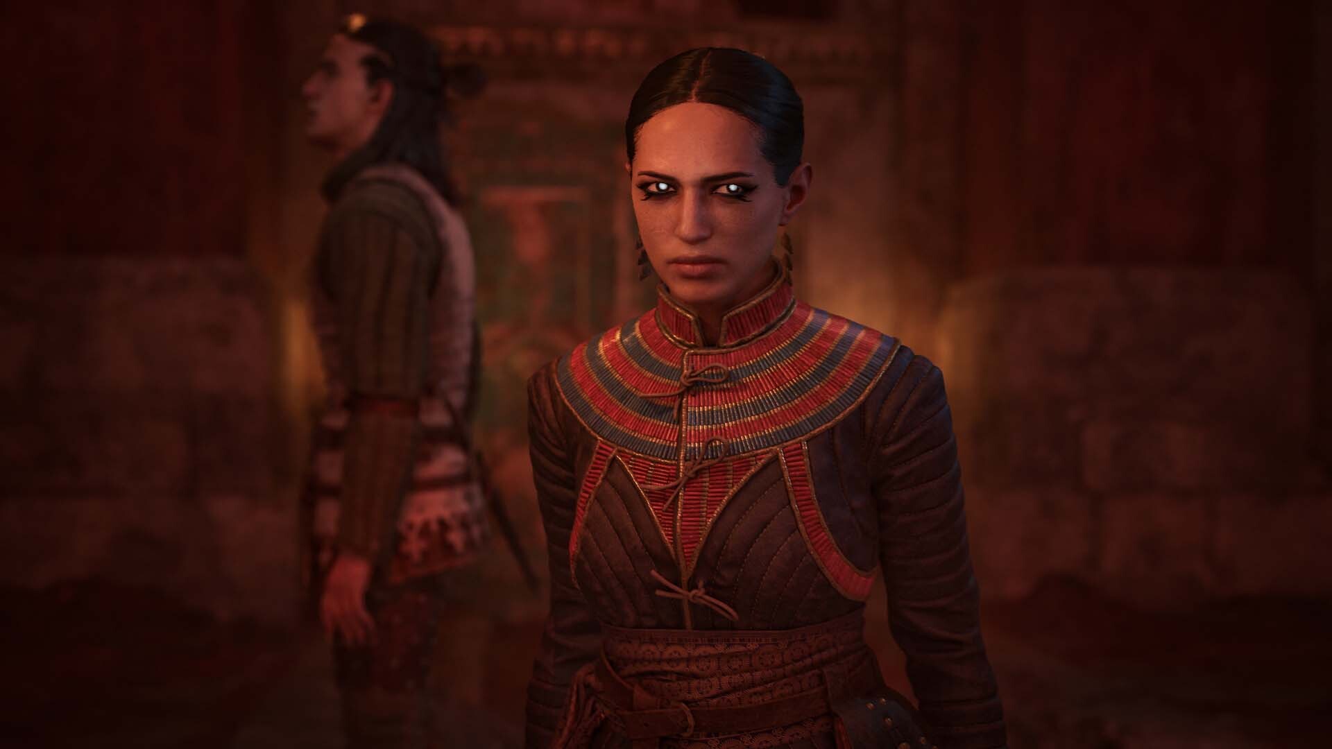 A pale-eyed vampire woman in Egyptian regalia faces the camera while Coen stands blurred behind her